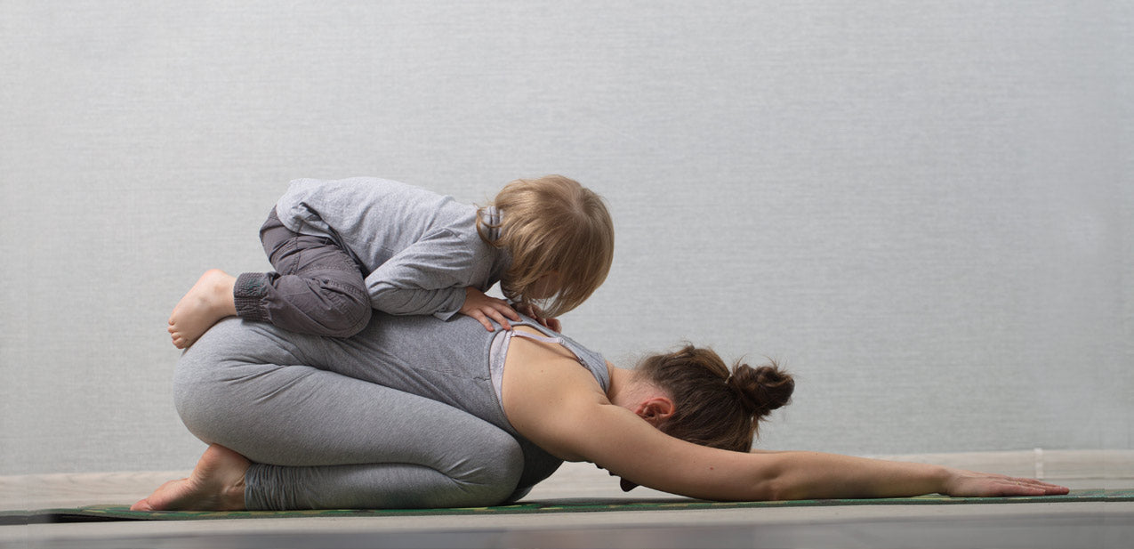 Mother in child pose with toddler on her back | TRIBE Yoga